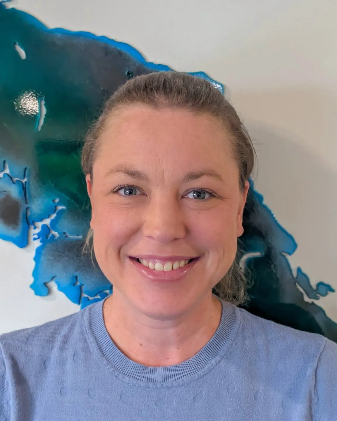 Dr. Jenna Jacobson, smiling, in front of a blue resin map of Vancouver Island